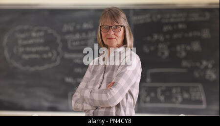 Certains enseignants senior woman with arms crossed standing in front of chalkboard Banque D'Images