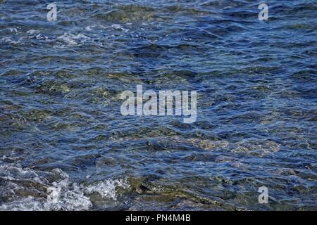 Vaguelettes sur la surface texturée de l'eau peu profonde, sur une plage. Rocks montrant juste sous la surface. Banque D'Images
