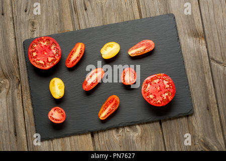 Variété de tomates fraîches mûres jardinage biologique différents types et couleurs spot avec de l'eau et les feuilles de basilic dans le bac en bois sur fond de bois gris ancien. Mise à plat, de l'espace Banque D'Images