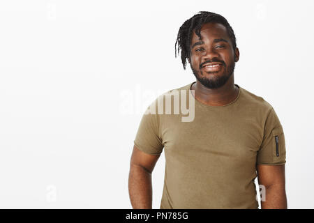 Jusqu'à la taille de balle sortant de charme african american guy avec barbe et moustache en t-shirt militaire, tout sourire et debout contre l'arrière-plan gris, d'être heureux tout en parlant à la fille Banque D'Images