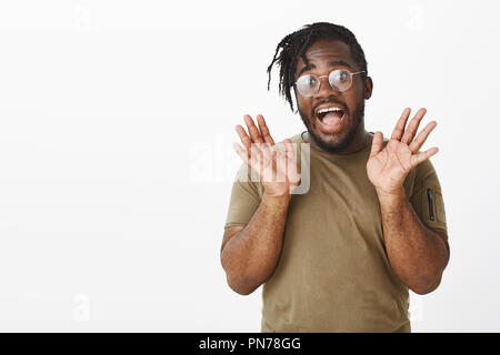 Portrait de l'homme à la peau sombre émotionnelle avec barbe dans les verres, tout sourire et levage palms près de face, d'être surpris et heureux de satisfaire la surprise, l'article enthousiaste sur fond gris Banque D'Images