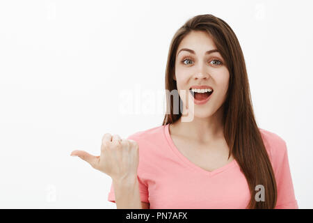 Tourné à l'intérieur de l'adorable femme brune en rose t-shirt, pointant vers la gauche avec le pouce et souriant joyeusement, d'être impressionné et étonné par l'excellent rendement des musiciens de rue Banque D'Images