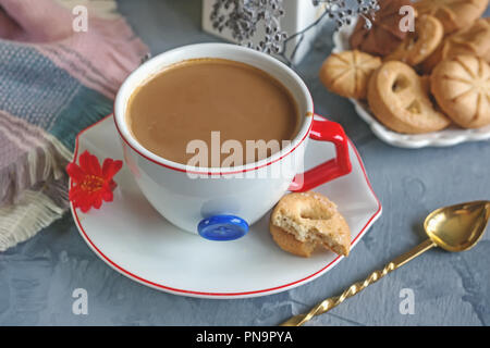 Chocolat chaud le matin dans la tasse blanche originale avec un bouton bleu sur le fond de biscuits. Le petit-déjeuner revigorant. Banque D'Images