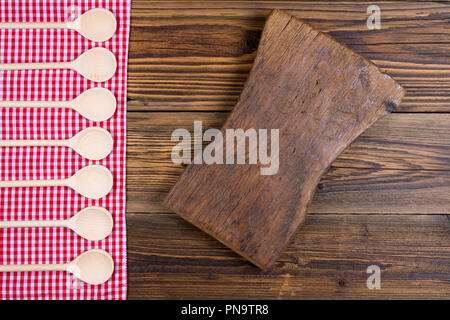 Vieux fond rustique en bois avec tissu à carreaux rouge blanc. Sur le tissu sont la cuisine en bois cuillères en une ligne. Avec l'exemplaire de l'espace sur une vieille planche à découper Banque D'Images