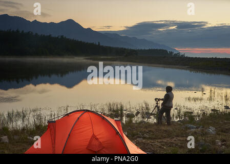 Photographe de prendre une photo du magnifique lac et montagne près de orange tente. Banque D'Images