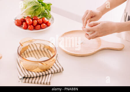 Les mains, c'est le bombardement des oeufs de poule. La femme prépare le petit-déjeuner à la maison. Les œufs de la poule au pot dans un sombre bois ware sur table. La tonalité Vintage Banque D'Images