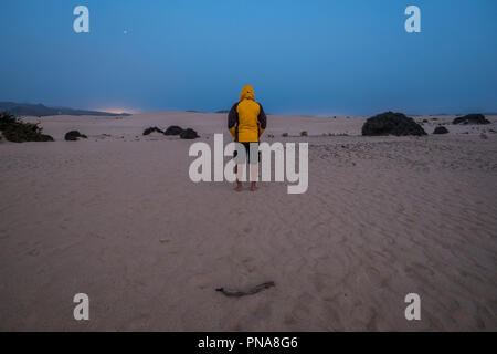 Homme seul avec yello jacket attendre et se tenir au milieu du désert de Corralejo Fuerteventura par nuit dans la soirée. froid et profiter de la natu Banque D'Images