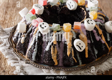 Halloween dessert : Gâteau bundt sombre avec des fruits confits, guimauve et glacis colorés sur la table horizontale. Banque D'Images