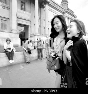 Deux jeunes femmes japonaises à l'adoption de la National Gallery, Trafalgar Square, Londres, Angleterre, Royaume-Uni. St Martin dans les champs derrière l'église Banque D'Images