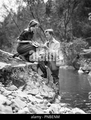 COUPLE DE PÊCHE 1920 HOMME DEBOUT DANS LE RUISSEAU HELPING WOMAN ON ROCKY BANQUE AVEC SA LIGNE - un HAR3386001 HARS COOPÉRATION PÊCHE MID-ADULT MID-ADULT MAN TOGETHERNESS WOMAN NOIR ET BLANC DE L'ORIGINE ETHNIQUE CAUCASIENNE HAR001 old fashioned Banque D'Images