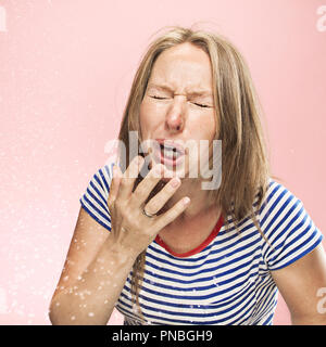 Jeune femme drôle de pulvérisation avec éternuements et quelques petites gouttes, studio portrait sur fond rose. Bande dessinée, caricature, l'humour. la maladie, l'infection, d'ACHE. Concept de santé Banque D'Images