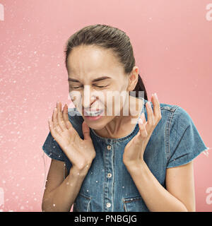 Jeune femme drôle de pulvérisation avec éternuements et quelques petites gouttes, studio portrait sur fond rose. Bande dessinée, caricature, l'humour. la maladie, l'infection, d'ACHE. Concept de santé Banque D'Images