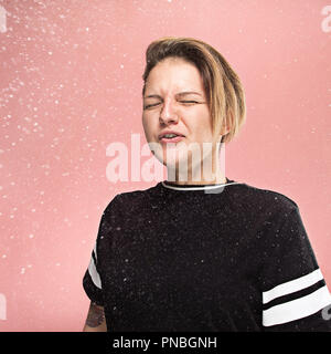 Jeune femme drôle de pulvérisation avec éternuements et quelques petites gouttes, studio portrait sur fond rose. Bande dessinée, caricature, l'humour. la maladie, l'infection, d'ACHE. Concept de santé Banque D'Images