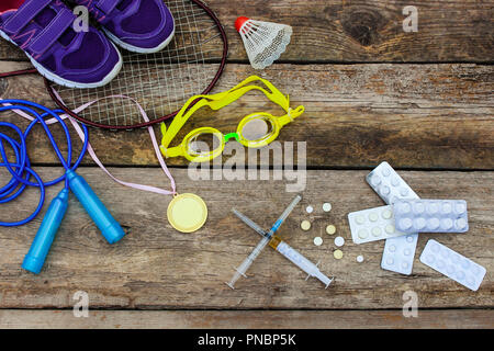 Équipements sportifs : racket, le saut à la corde, lunettes de natation, des chaussures de sports, médaille et médicaments sur fond de bois. Image tonique Banque D'Images