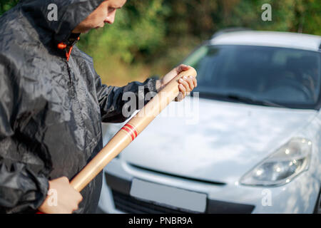 La personne agressive avec la batte de baseball à l'avant du véhicule Banque D'Images