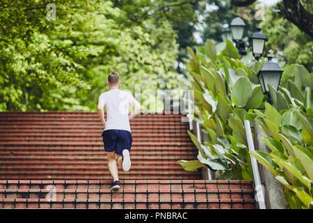 Sport dans la ville. Jeune homme courir vers le haut escalier extérieur en parc public. Banque D'Images