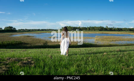 Retour d'une jeune femme mariée Brunette avec de longs cheveux bouclés portant jupe blanche marcher dans un paysage à côté d'un lac Banque D'Images