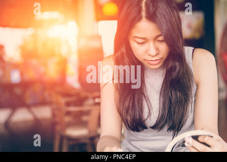 Profitez de moments de détente avec lecture du livre, la femme asiatique teen thaï à l'accent grave lire livre de poche dans un café le matin, le ton des couleurs vintage Banque D'Images