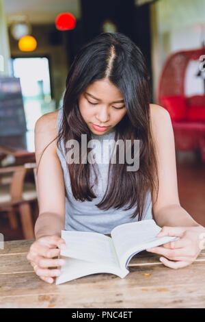 Profitez de moments de détente avec lecture du livre, la femme asiatique teen thaï à l'accent grave lire livre de poche dans un coffee shop. Banque D'Images