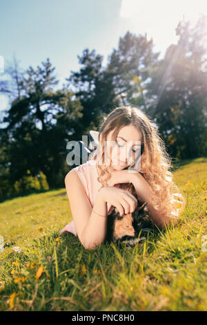 Girl lying on grass avec cat. Printemps ou été concept par temps chaud. Arrière-plan flou. Ginger kitten avec deux visage masque de couleur. Banque D'Images