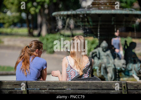 Deux femmes s'asseoir sur le banc à la fontaine et parlez. Banque D'Images