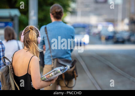 Femme sur le casque à l'écoute de la musique et en attente d'un arrêt de tramway. Banque D'Images