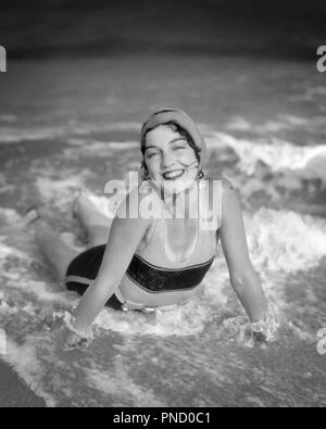 Années 1920 SMILING BRUNETTE WOMAN LYING IN BEACH SURF VAGUES PORTANT BONNET DE MAILLOT 1 LOOKING AT CAMERA - b5831 HAR001 HARS CHERS PERSONNES SURF B&W EYE CONTACT CÔTE BRUNE JOYEUX BONHEUR STYLES ANGLE HAUTE EXCITATION PLAGES LOISIRS ÉLÉGANT MAILLOT DE JOYEUX SOURIRES FASHIONS SEASHORE YOUNG ADULT WOMAN NOIR ET BLANC DE L'ORIGINE ETHNIQUE CAUCASIENNE HAR CÔTIÈRES001 old fashioned Banque D'Images