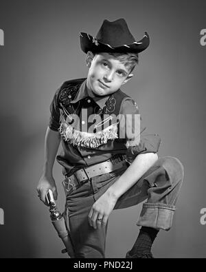 1950 BOY WEARING COWBOY HAT FRANGÉ WESTERN SHIRT ÉTUI EN CUIR ET LA COURROIE À LA CAMÉRA À MAIN SUR SIX SHOOTER - PISTOLET PAC j4224 DEB001 HARS, CONTACT AVEC LES YEUX SUR LES RÊVES DE L'IMAGINATION DES ARMES À FEU DEB001 élégant Revolver de pistolet de tir à franges juvéniles 6 NOIR ET BLANC à l'ANCIENNE Origine ethnique Caucasienne Banque D'Images
