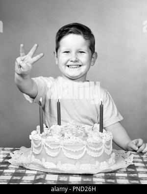 1950 FIER SMILING BOY LOOKING AT CAMERA WITH BIRTHDAY CAKE HOLDING UP trois doigts pour son âge - j6179 HAR001 H.A.R.S. B&W EYE CONTACT CÉLÉBRER BONHEUR SON EXCITATION L'OCCASION DE CROISSANCE JOYEUX SOURIRES JUVÉNILES NOIR ET BLANC DE L'ORIGINE ETHNIQUE CAUCASIENNE HAR001 old fashioned Banque D'Images