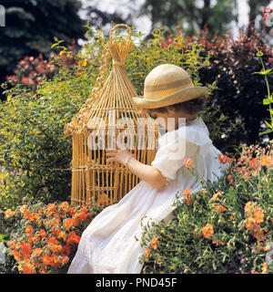 1970 Petite BLONDE FILLE AVEC ROBE BLANCHE ET CHAPEAU DE PAILLE à la cage à oiseaux en osier à vide en jardin de fleurs sauvages aux couleurs vives - kj7575 PHT001 HARS DE PERSONNES DISPARUES EN OSIER COLORÉ LIBERTÉ BIENVEILLANTE TRISTESSE BONHEUR RÊVES ET DE FLEURS SAUVAGES DANS LE CADRE À CHAPEAU DE PAILLE CONCEPTUEL ÉCHAPPER JEUNE PRINTEMPS élégant à l'ANCIENNE Origine ethnique Caucasienne Banque D'Images