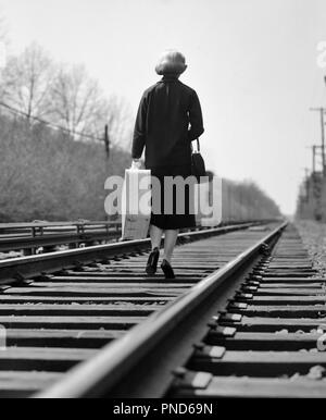 Années 1950 Années 1960 femme battue à l'appareil photo s'échapper en marchant sur des voies de chemin de fer TRANSPORTANT VALISE LAISSANT - s10060 DEB001 HARS PERSONNES PLEINE LONGUEUR DES SYMBOLES RISQUE LAISSER B&W TRISTESSE LES VOIES SEULE FIGURE LA LIBERTÉ VICTIME D'EMBALLEMENT CHOIX COURAGE FORCE FED UP DIRECTION DE L'HOMME BLESSÉ FINI MAL dos à la caméra fait échapper CONCEPTUEL SURVIVANT SURVIVRE DEB001 MI-ÉTÉ BATTUES SYMBOLIQUE DES PROFILS MID-ADULT WOMAN SYNDROME ADULTES gens misérables désespérés NOIR ET BLANC SAC À MAIN LA REPRÉSENTATION À L'ANCIENNE Banque D'Images
