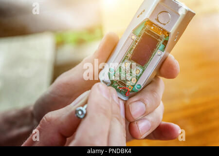 Les mains de l'homme moderne fixation vaporizer e-cig gadget à vape e-liquide. L'entretien de l'équipement électronique mech mod vaping périphérique. Vaper, réparation de l'appareil Banque D'Images