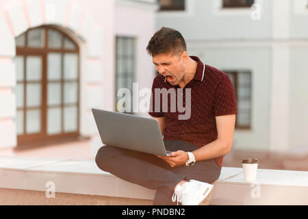 Young businessman blogger man behind laptop et crier dans la ville. Le concept d'émotions agressives. Perte Banque D'Images
