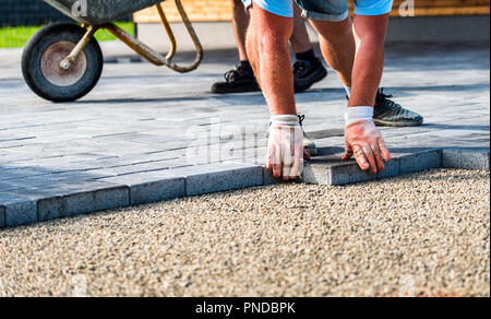 La pose des dalles de béton gris en chambre courtyard entrée patio. Les travailleurs professionnels maçons sont l'installation de nouveaux carreaux ou dalles pour allée, Banque D'Images