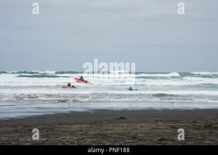 Piha beach, Auckland, Nouvelle-Zélande - le 17 décembre 2016 : la kayakiste bravant la mer de Tasman rugueux avec maître nageur à Piha beach à Auckland, en Nouvelle-Zélande. Banque D'Images