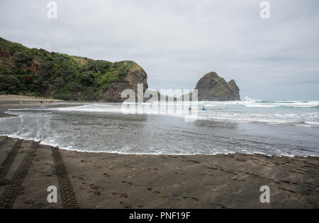 Piha beach, Auckland, Nouvelle-Zélande - le 17 décembre 2016 : la kayakiste et surfer le long de la côte de la mer de Tasman rugueuse à Piha beach à Auckland, en Nouvelle-Zélande. Banque D'Images