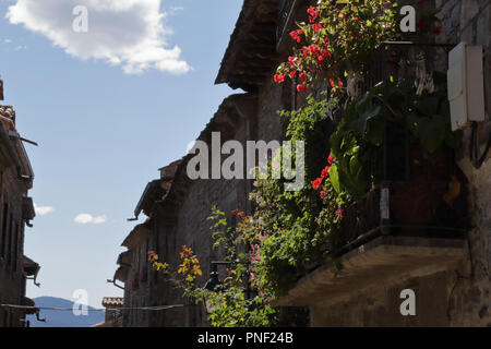 Voici quelques unes des maisons traditionnelles avec un balcon en pierre rouge, fleurs et feuilles vertes sur fond bleu ciel nuageux dans la ville rurale médiévale Ainsa, Espagne Banque D'Images