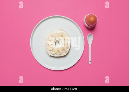 La moitié de bagel avec fromage à la crème et un oeuf dur sur une plaque blanche sur fond rose avec une cuillère blanc avec espace pour copier et texte Banque D'Images