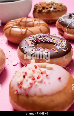 Assortiment de beignets sur un fond rose pastel avec une tasse de café dans l'arrière-plan. Avec anneau chocolat comprend arrose ainsi que divers autres Banque D'Images