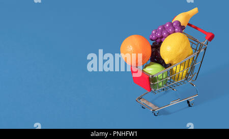 Toy panier chariot rempli de fruits et légumes en plastique sur un fond bleu avec l'espace pour copier et texte Banque D'Images