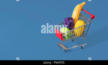 Toy panier chariot rempli de fruits et légumes en plastique sur un fond bleu avec l'espace pour copier et texte Banque D'Images