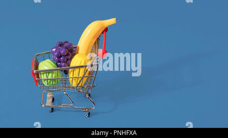 Toy panier chariot rempli de fruits et légumes en plastique sur un fond bleu avec l'espace pour copier et texte Banque D'Images