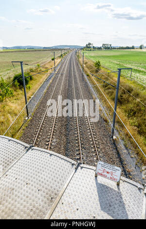 Un réseau ferroviaire à grande vitesse avec l'équipement de lignes aériennes (poteaux, caténaires et lignes électriques) pour la fourniture de trains et un signe de danger dans l'avant-plan. Banque D'Images