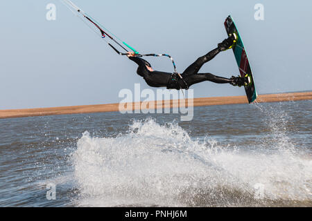 Kiteboarder tirant d'air et d'obtenir des astuces sur un jour d'été parfait avec ciel bleu clair. Strret bardeaux, Suffolk, UK Banque D'Images