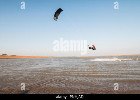Kiteboarder tirant d'air et d'obtenir des astuces sur un jour d'été parfait avec ciel bleu clair. Strret bardeaux, Suffolk, UK Banque D'Images