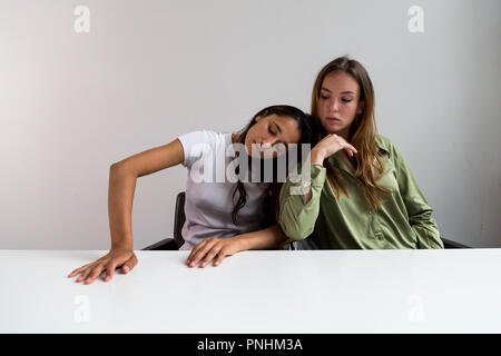 Deux femmes effectuant des poses artistiques assis à grand bureau. La tête penchée sur l'épaule. Plan moyen. Sur face avant. Banque D'Images