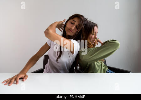 Deux femmes effectuant des poses artistiques assis à grand bureau. Dos à Dos. Plan moyen. Sur face avant. Banque D'Images