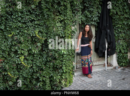 Femme debout devant un mur de lierre en sarong avec grand parapluie noir à côté d'elle Banque D'Images