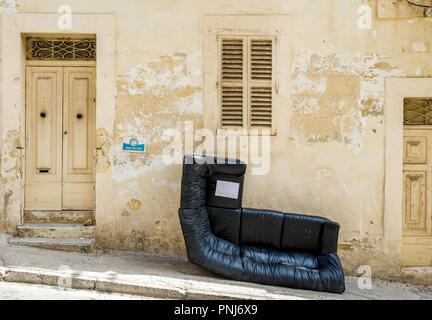 Cuir noir désaffectées corner chaise placée sur la chaussée à Sliema, Malte prêt à être recueillies. Banque D'Images