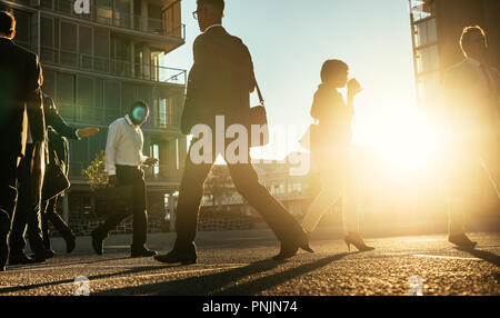 Hommes et femmes se rendre au bureau tôt le matin transportant des sacs de bureau avec sun flare en arrière-plan. Businesswoman walking sur une ville occupée str Banque D'Images